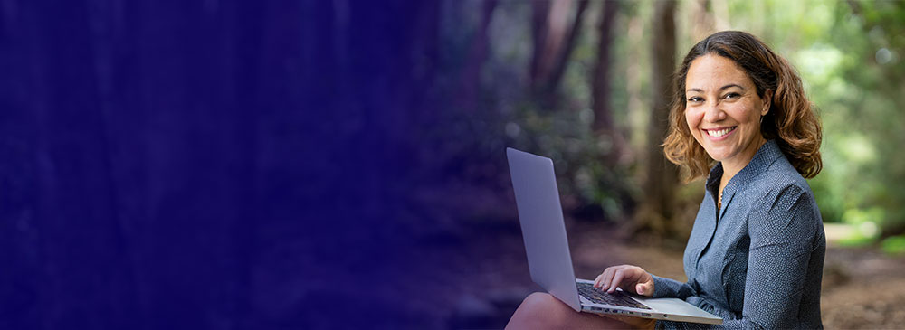 Lady sitting in the forest on a laptop looking into the camera